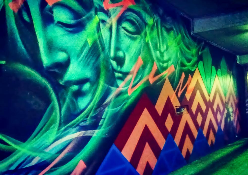 Shot of a concrete wall with large street art painted on it depicting three green female faces in portrait view.