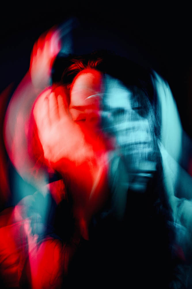 Abstract image depicting the ADHD inner monologue. Photo of several very blurry faces and hands merging, in different colours (red and grey), depicting chaos.