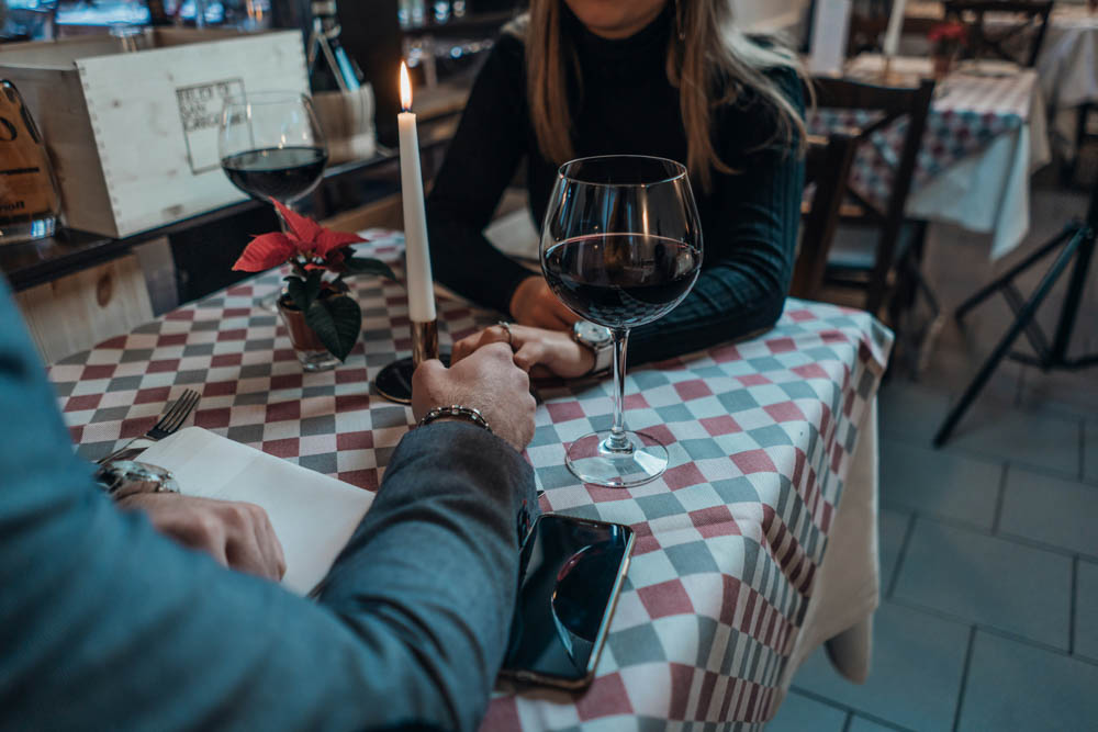 Photo of a man and a woman eating at a restaurant, holding hands with a lit candle on the table and wine glasses.