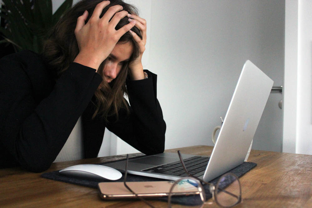ADHD and perfectionism. Photo of a woman looking at a laptop with her head in her hands looking frustrated and overwhelmed. 