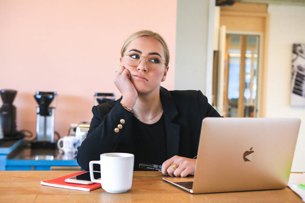 Photo of a woman in business attire, sitting infront of a laptop with her head resting on her hand looking unimpressed.