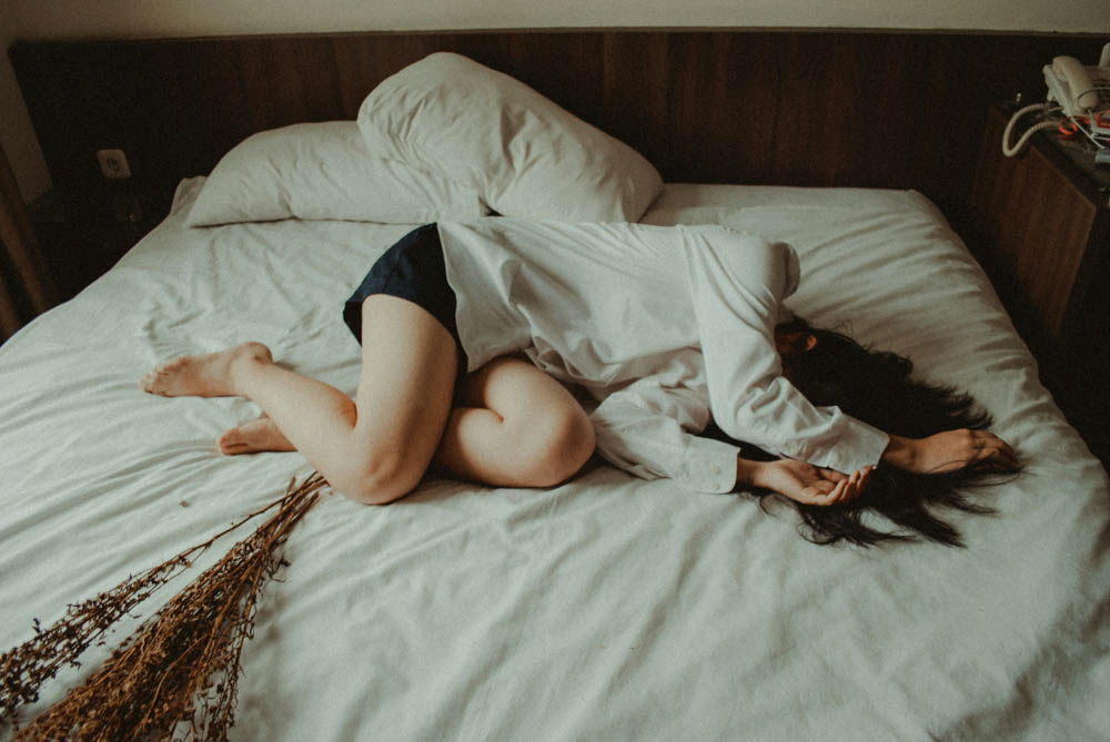 Photo of a woman that is addicted to the narcissist, lying on her bed covering her face.