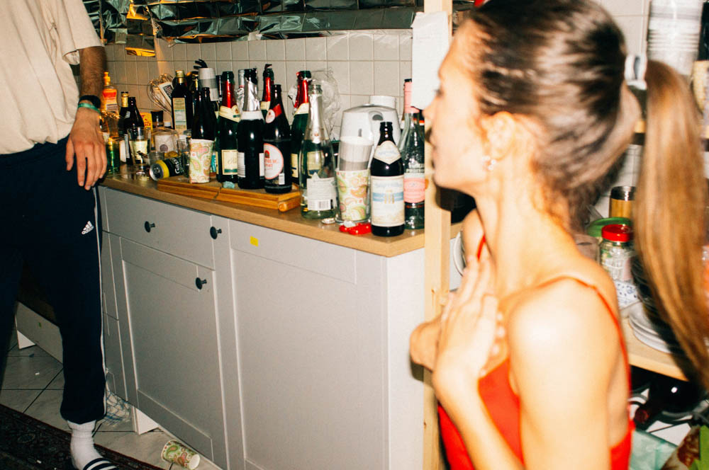 Photo of a young lady at a party, surrounded by bottles of alcohol.