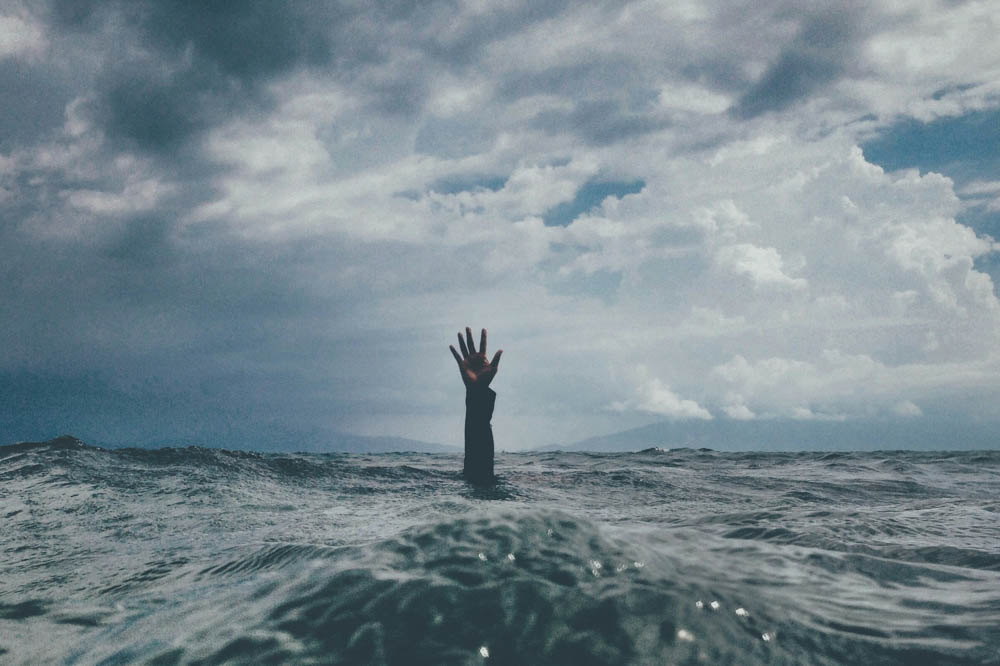 Photo of a persons arm sticking out of the ocean, depicting stress and overwhelm.