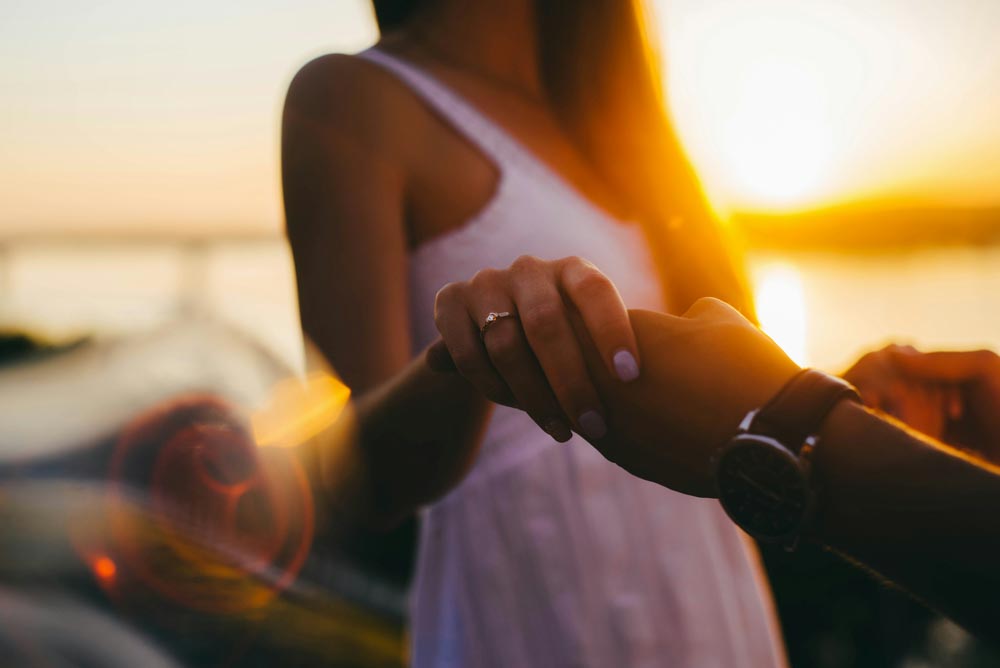 Photo of a man an woman holding hands with the sun setting in the background. 23 Adorable Signs He's the One For You.