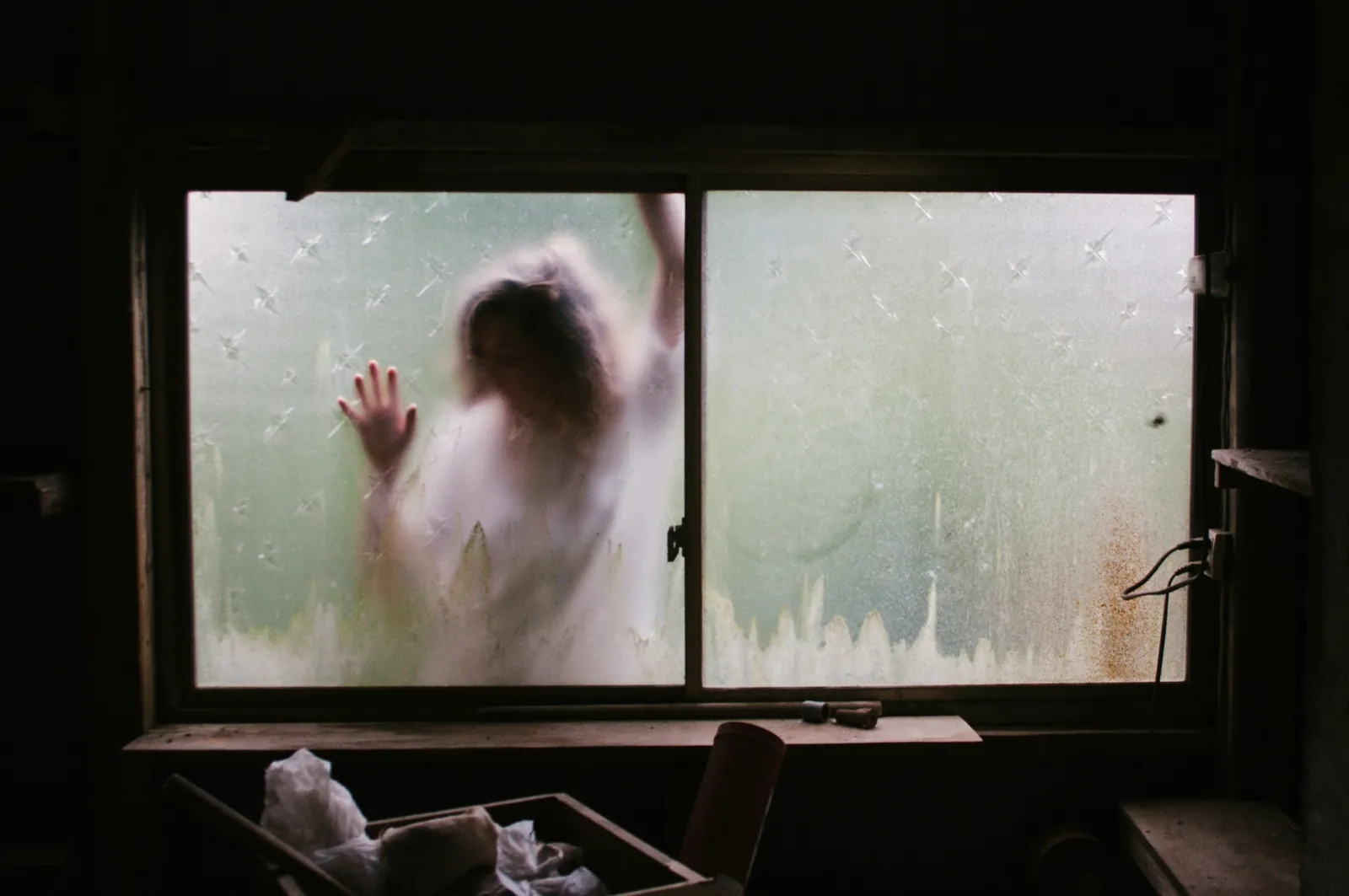 Blurred silhouette of a woman pressing her hand against a frosted window, symbolising the emotional isolation of feeling addicted to the narcissist.
