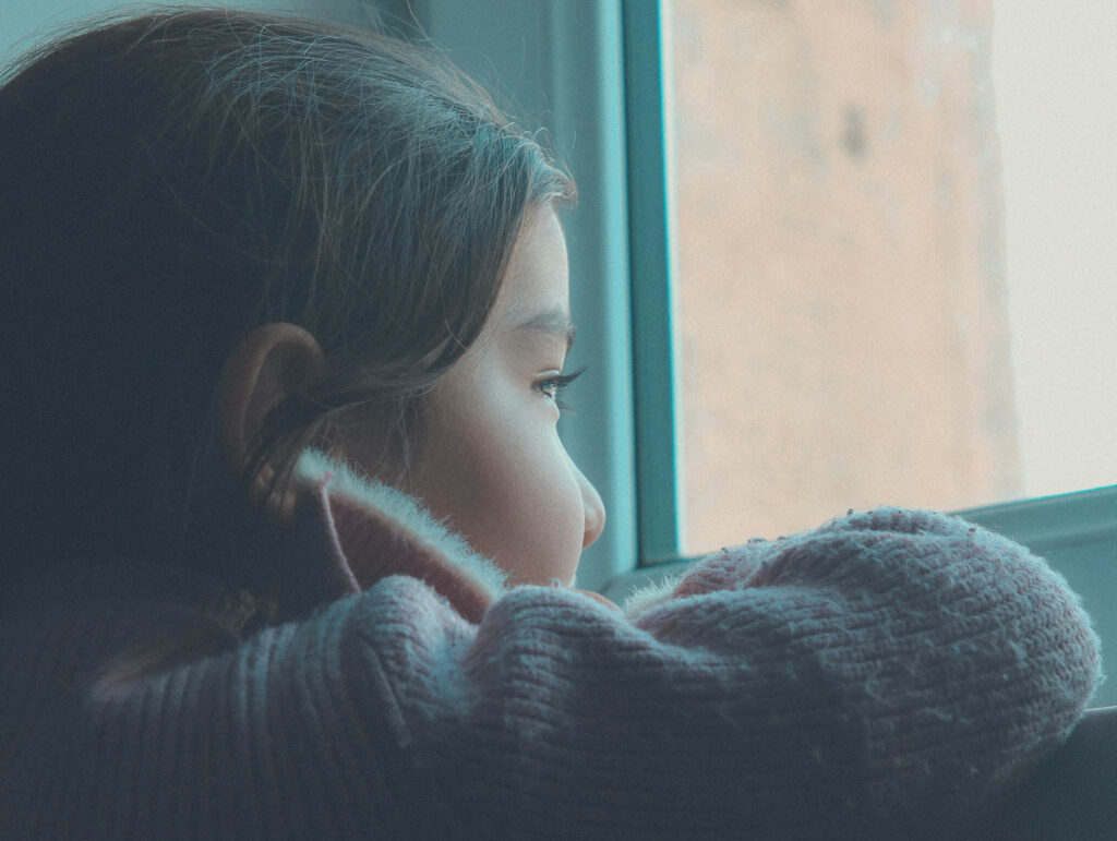 Child looking out a window, representing the lasting effects of childhood abandonment