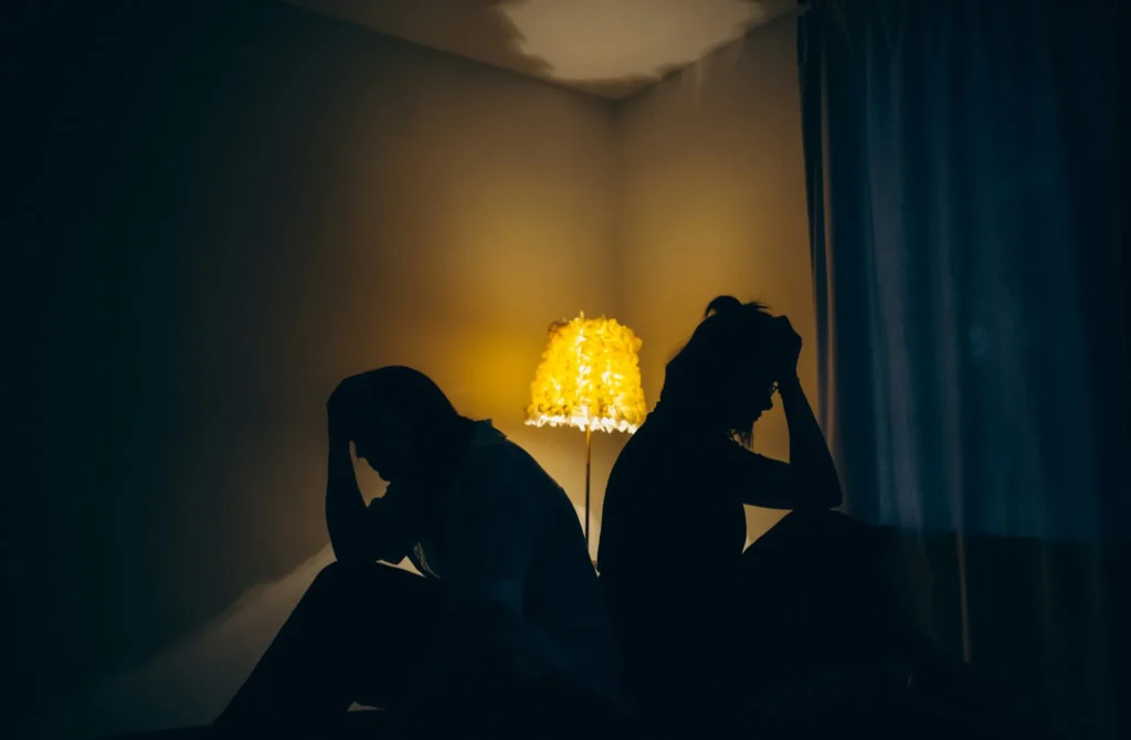 Two people sitting back to back in a dimly lit room, illustrating emotional distance in a relationship affected by dark empath manipulation.