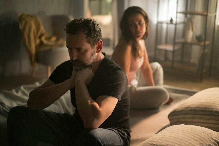 Couple sitting apart on a sofa, appearing emotionally distant from each other