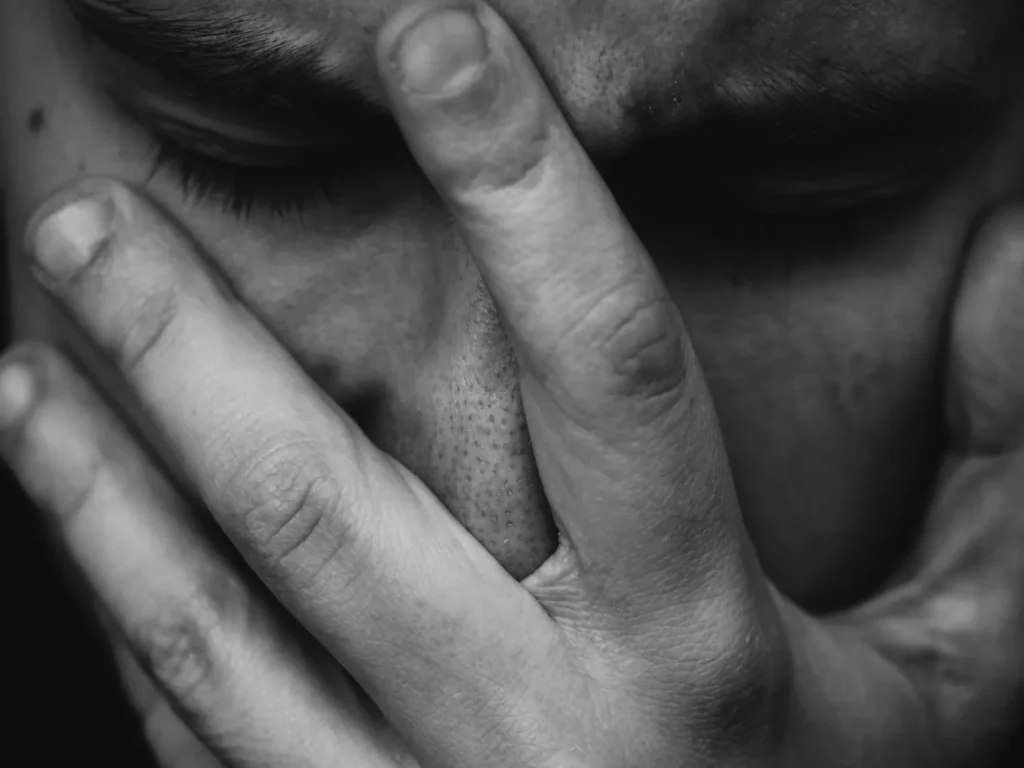 Trauma bonding and emotional distress illustrated by a black-and-white close-up of a man covering his face with his hand.